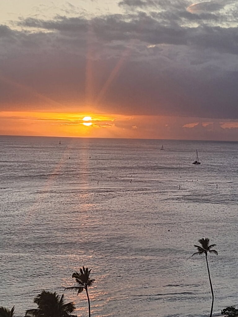 A serene sunset over the ocean, featuring distant sailboats silhouetted against the vibrant sky.