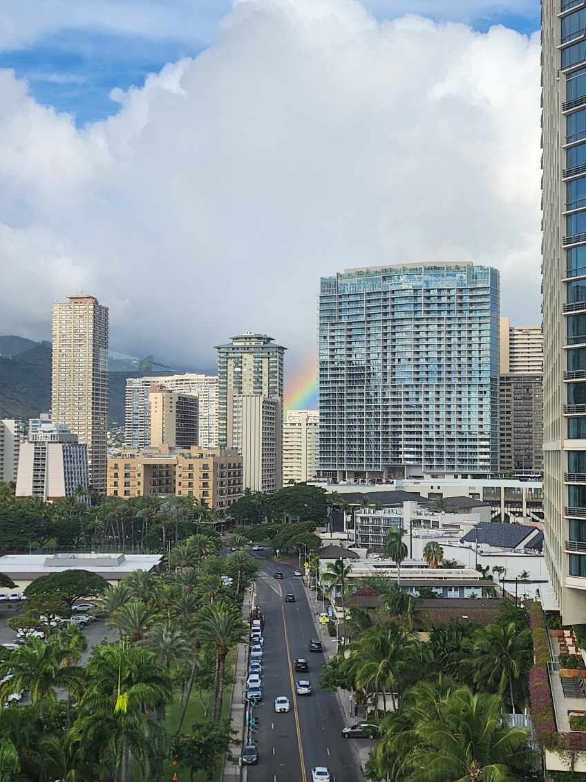 A colorful rainbow spans the sky above a city, creating a striking contrast against the buildings below.